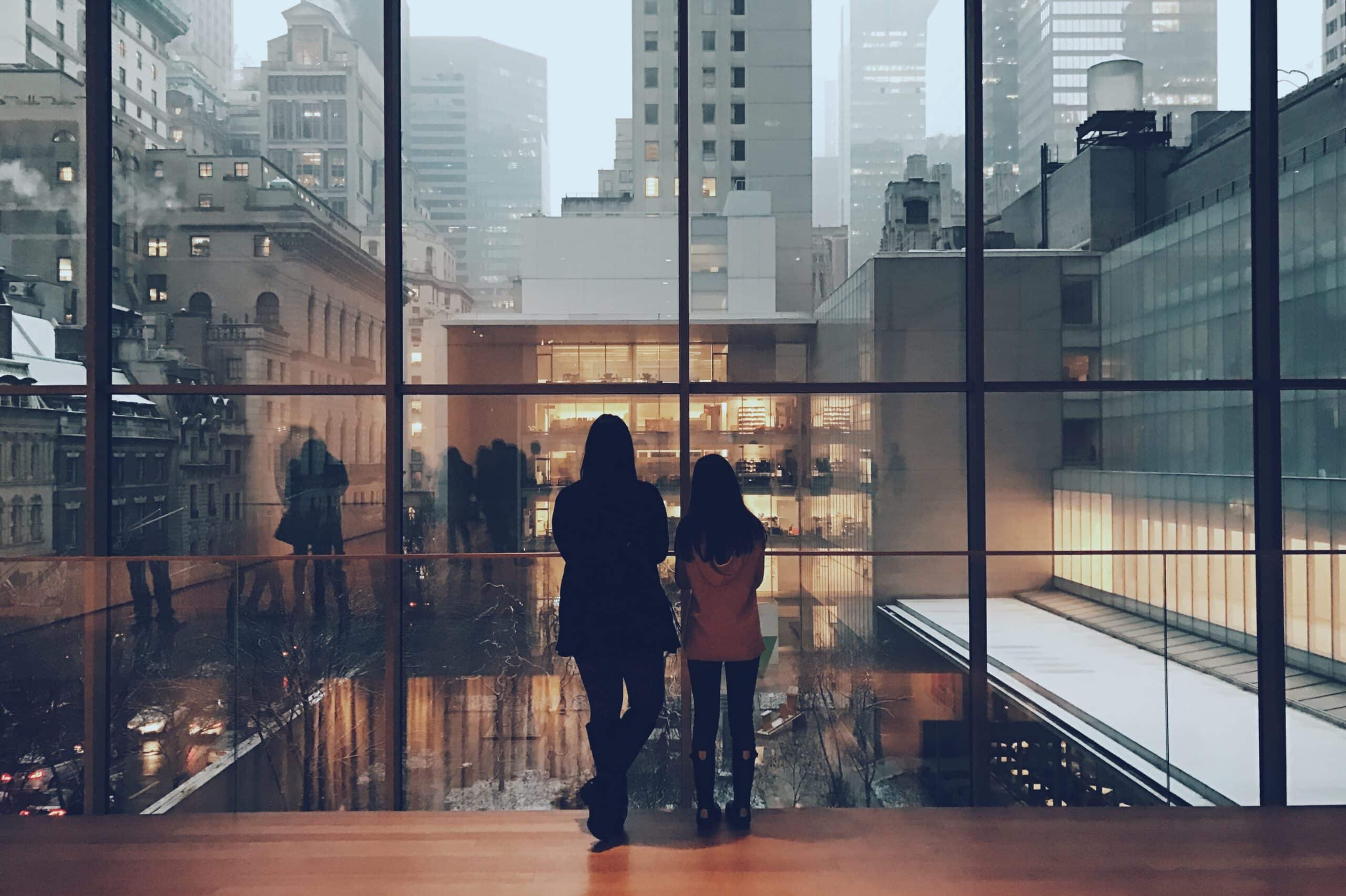 IT FM wide shot of two females standing at a huge glass window looking at the view of high rise buildings